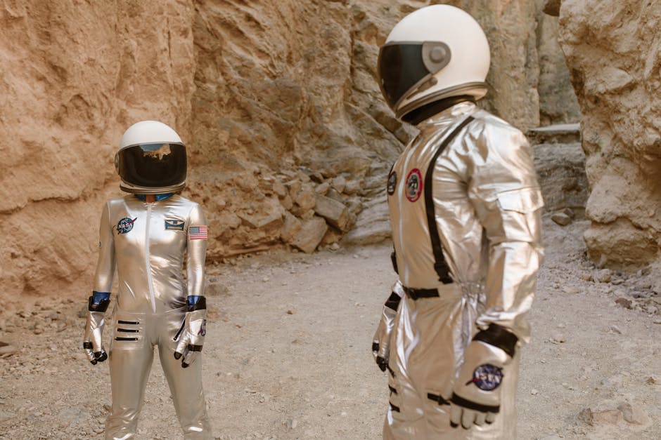 Two astronauts in silver space suits exploring a rocky, desert-like environment, resembling Mars.